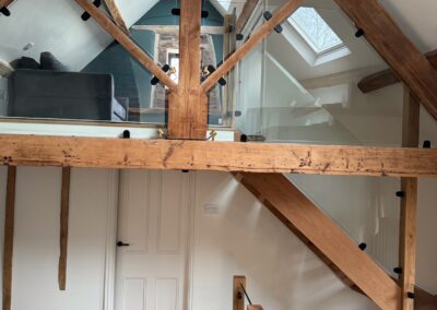 A modern oak stair case with a glass balustrade with exposed oak beams in a barn conversion