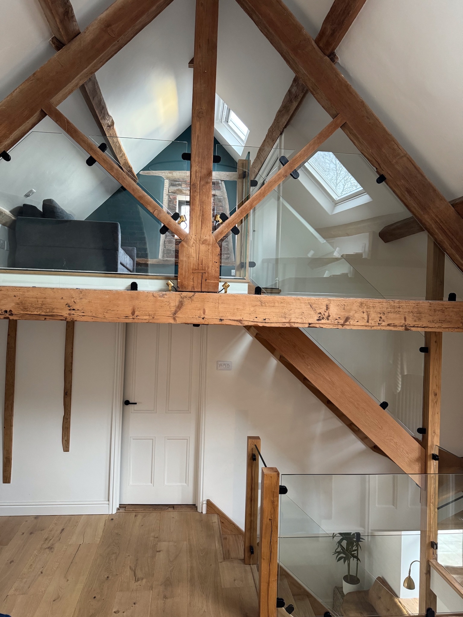 A modern oak stair case with a glass balustrade with exposed oak beams in a barn conversion