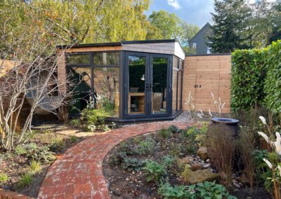Reclaim brick path surrounded by autumnal planting leading to a timber clad out door office